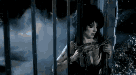 a woman is chained to a fence in a dark room and holding a chain .