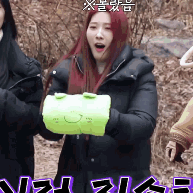 a woman in a black coat holds a green glove with a smiley face on it