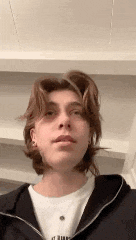 a young man with long hair is wearing a black hoodie and a white shirt .