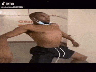 a shirtless man wearing a face mask is dancing in a hallway .