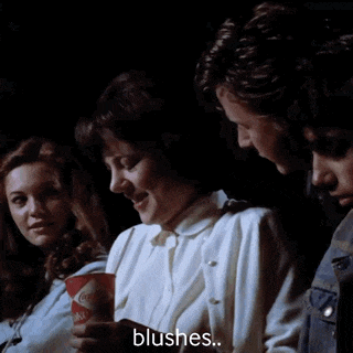a woman holding a cup of coca cola blushes while sitting in a dark room