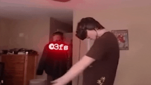a man wearing a virtual reality headset is standing in a room with a red hoodie that says 03f8 on it .