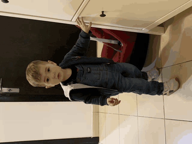 a young boy standing in front of a white dresser with his hand on the drawer