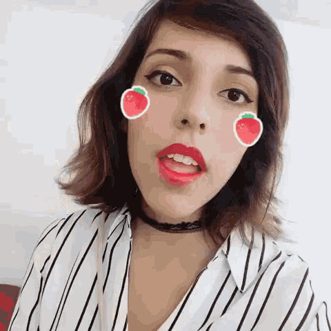 a woman wearing a choker and red lipstick is making a funny face with strawberries on her face .