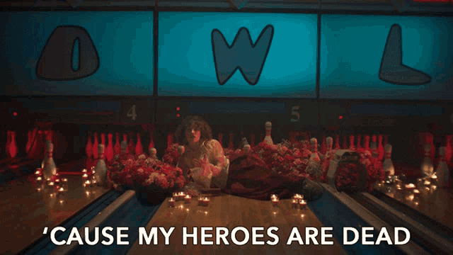 a woman is laying on a bowling alley with the words ' cause my heroes are dead ' below her