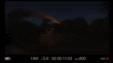 a video of a man standing in a field with a fire in the background is being recorded