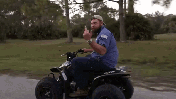 a man in a blue shirt is riding a honda atv