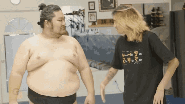 a man wearing a black t-shirt that says ' g ' on it talks to a sumo wrestler