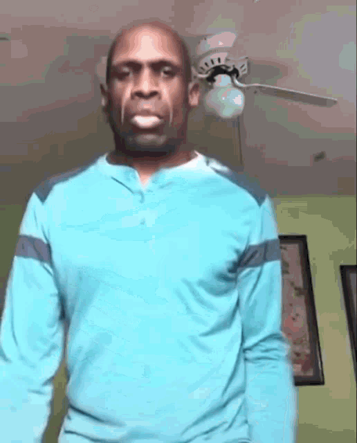 a man in a blue shirt is standing under a ceiling fan .