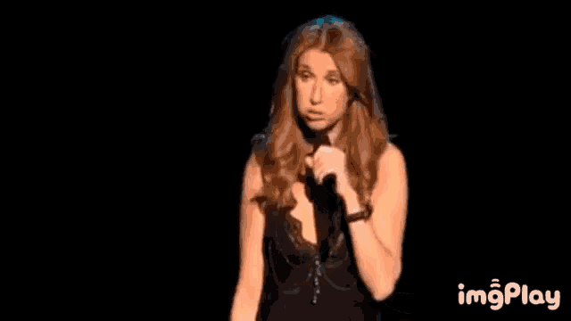 a woman in a black dress is standing on a stage in front of a black background with the words imgplay below her .