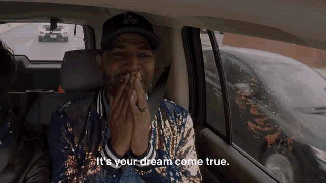 a man in a la hat is sitting in the back seat of a car with the words " it 's your dream come true "