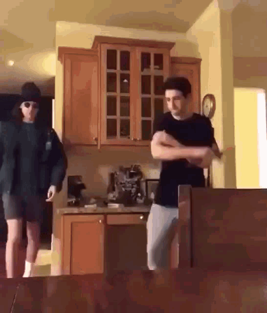 two men are dancing in a kitchen with a clock on the wall