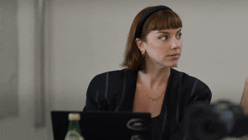 a woman wearing a headband sits in front of a laptop that has the letter g on it