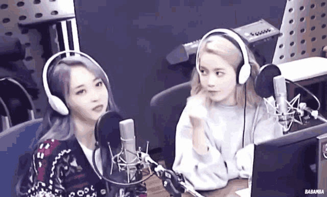 two women wearing headphones are sitting in front of microphones in a radio studio .