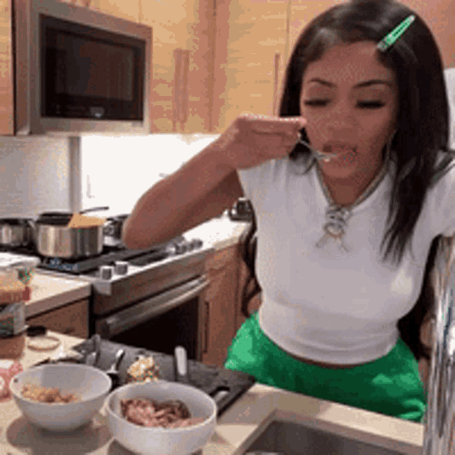 a woman in a white top and green shorts is eating from a bowl