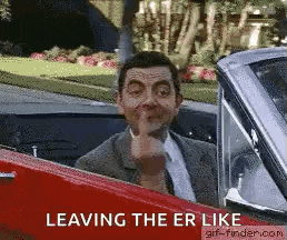 a man in a suit and tie is sitting in a red car and making a funny face .
