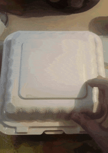 a person is opening a styrofoam container with a piece of paper on it