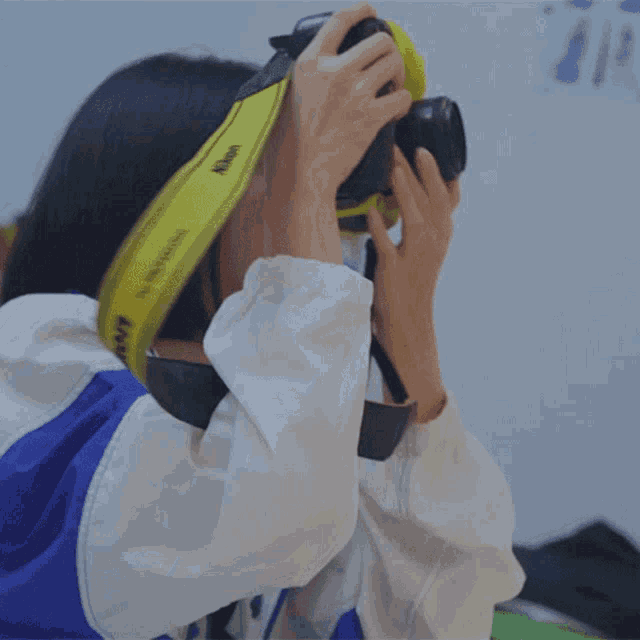 a woman in a blue and white jacket is holding a yellow canon camera