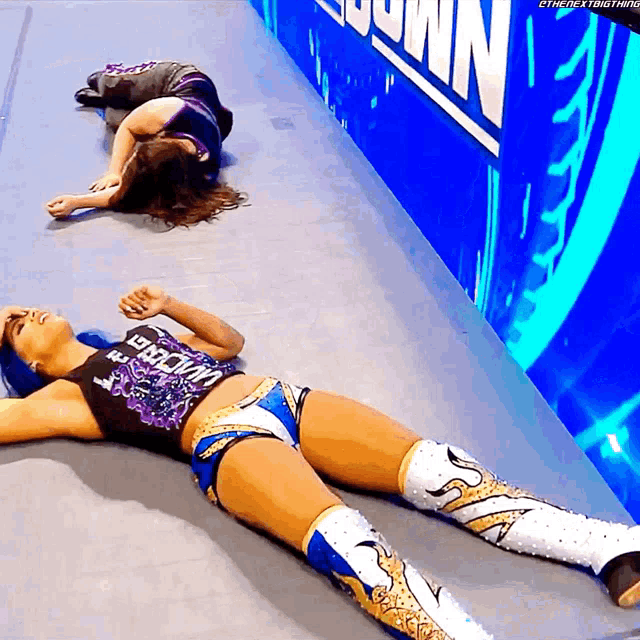 two female wrestlers are laying on the floor in front of a blue wall that says ' smackdown ' on it