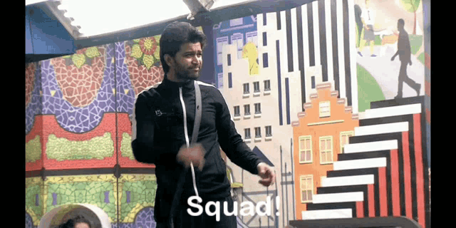 a man in a black jacket is dancing in front of a colorful wall with the word squad on it