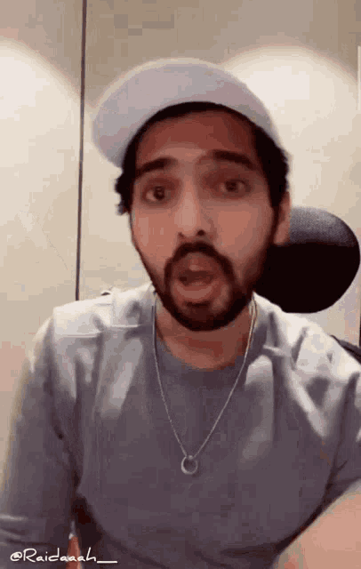 a man with a beard is wearing a hat and a necklace with the name raidaah on the bottom
