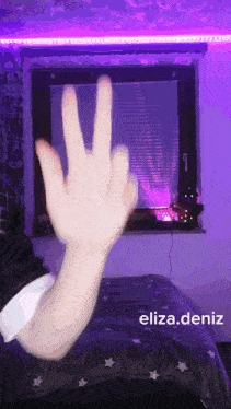 a person is making a peace sign with their fingers in front of a window with purple lights .