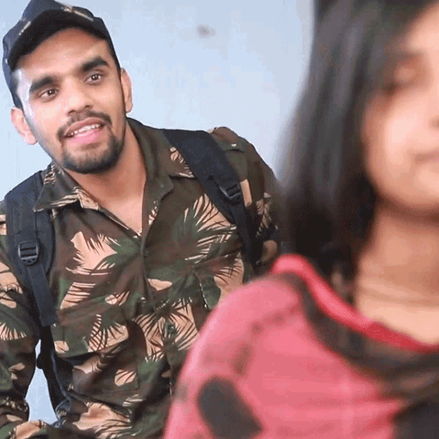 a man in a camouflage shirt is smiling while looking at a girl