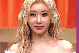 a close up of a woman 's face with blonde hair and a red curtain in the background .