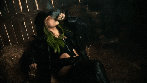 a woman with green hair is smoking a cigarette in a dark room