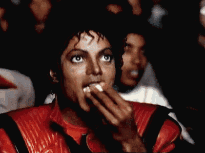 a man in a red leather jacket is covering his mouth with his hands while watching a movie .