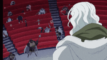 a man with long white hair stands in front of a crowd of people in red seats