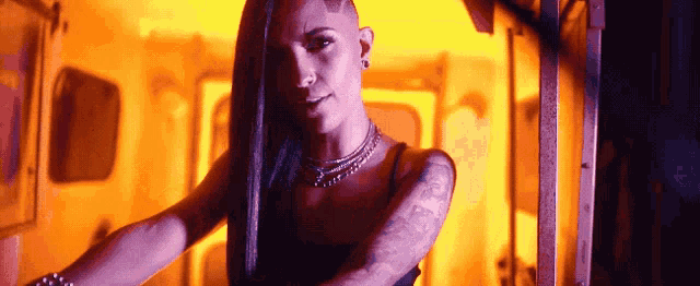 a woman with a shaved head and a tattoo on her arm stands in a dark room