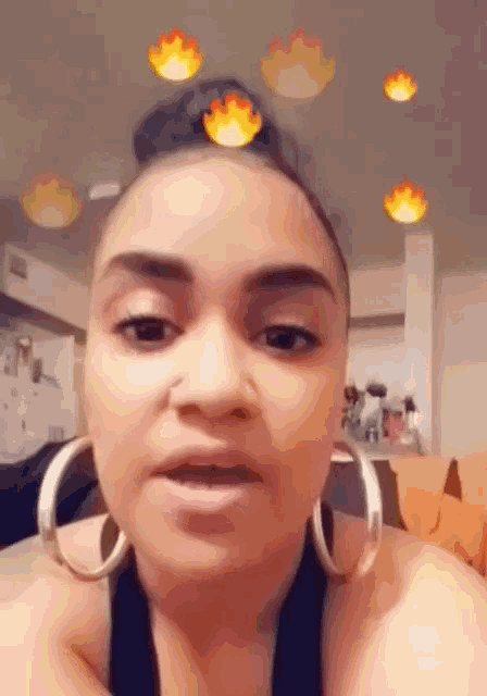 a woman wearing hoop earrings looks at the camera with flames behind her head