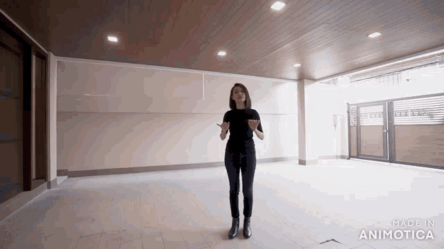a woman in a black shirt stands in an empty room with the words made in animotica on the bottom