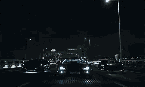 three cars are driving down a highway at night and one of them has a license plate that starts with the letter b