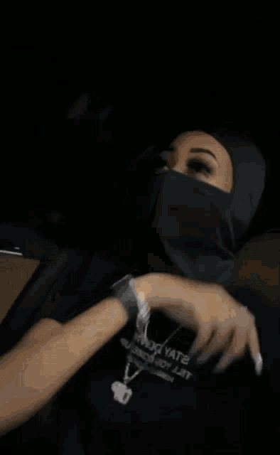 a woman wearing a mask and a necklace is giving a thumbs up sign .