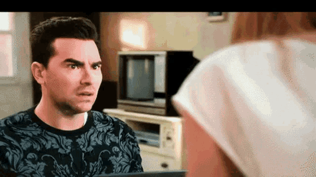 a man in a black and white shirt is talking to a woman in a living room .