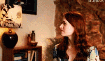 a woman with red hair is sitting at a table in a living room with a lamp .