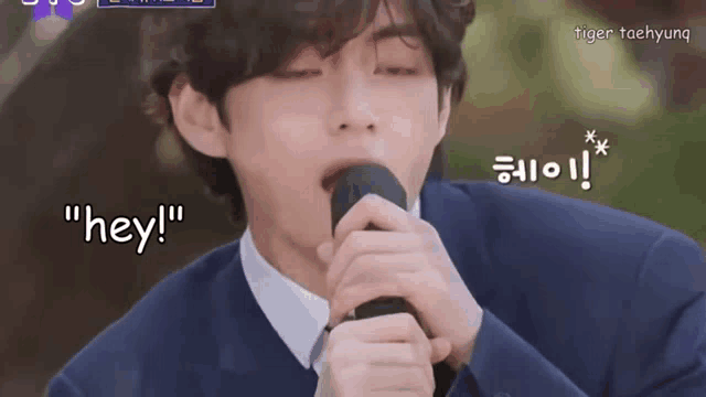 a man in a suit is singing into a microphone and says " hey " in korean