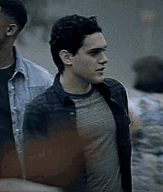 a young man in a plaid shirt and a denim jacket is standing next to another man .