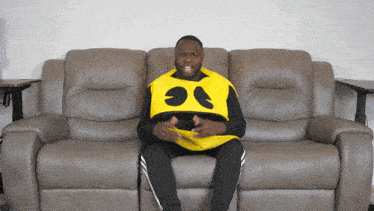a man is sitting on a couch wearing a yellow vest with a face on it