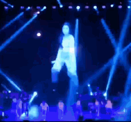 a group of people are dancing on a stage with blue lights behind them