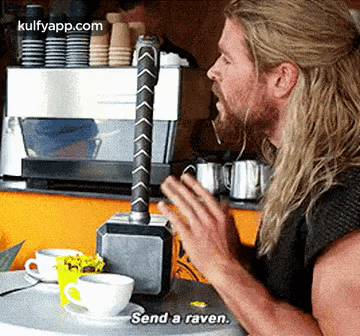 a man with long hair is sitting at a table with a hammer on it and a cup of coffee .