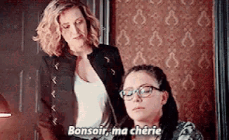 two women are standing next to each other in a room and one of them is talking in french .