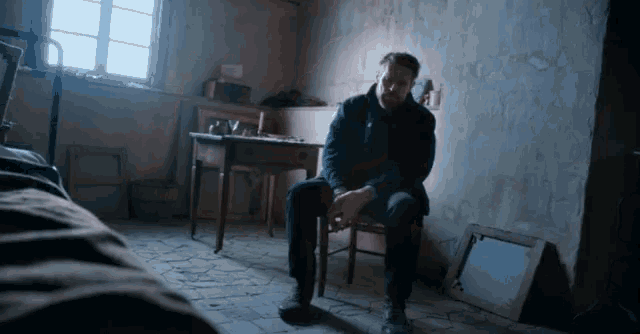 a man is sitting on a chair in a dark room with a window
