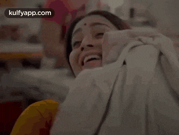 a woman is laughing while holding a pile of clothes in her lap .