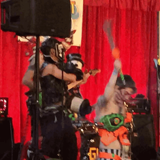 a man in a mask is playing a guitar in front of a red curtain with the letter f on it