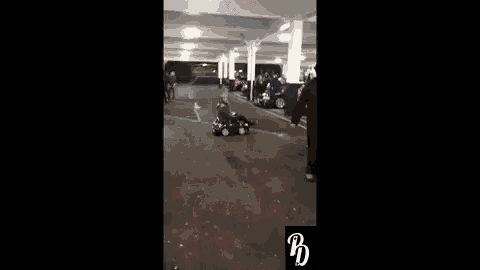 a man is driving a small red car in a parking garage .