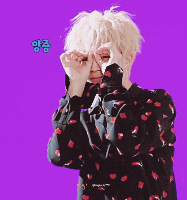 a person covering their eyes with their hands in front of a purple background with a foreign language written in blue
