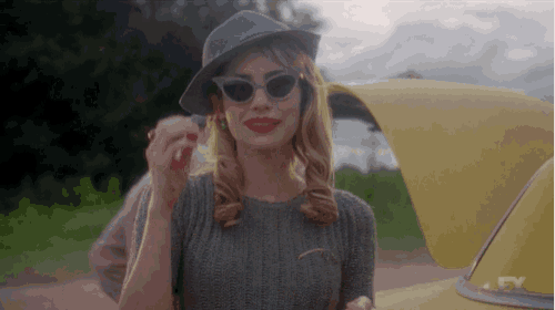 a woman wearing sunglasses and a hat is standing next to a yellow car